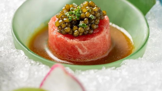 Green bowl with a pink dish topped with caviar on ice. Green leaf and radish garnish. Elegant and fresh dining presentation.