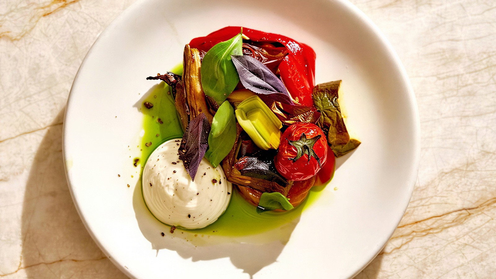 A plate with roasted red peppers, cherry tomatoes, herbs, and a dollop of white cream on a marble surface, in bright soft lighting.