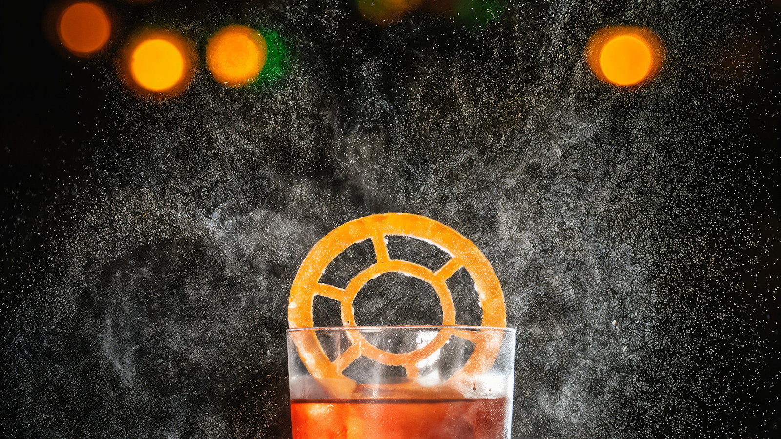 A glass of orange cocktail with a circular orange slice on a dark background, illuminated by warm, glowing bokeh lights, creating a festive mood.