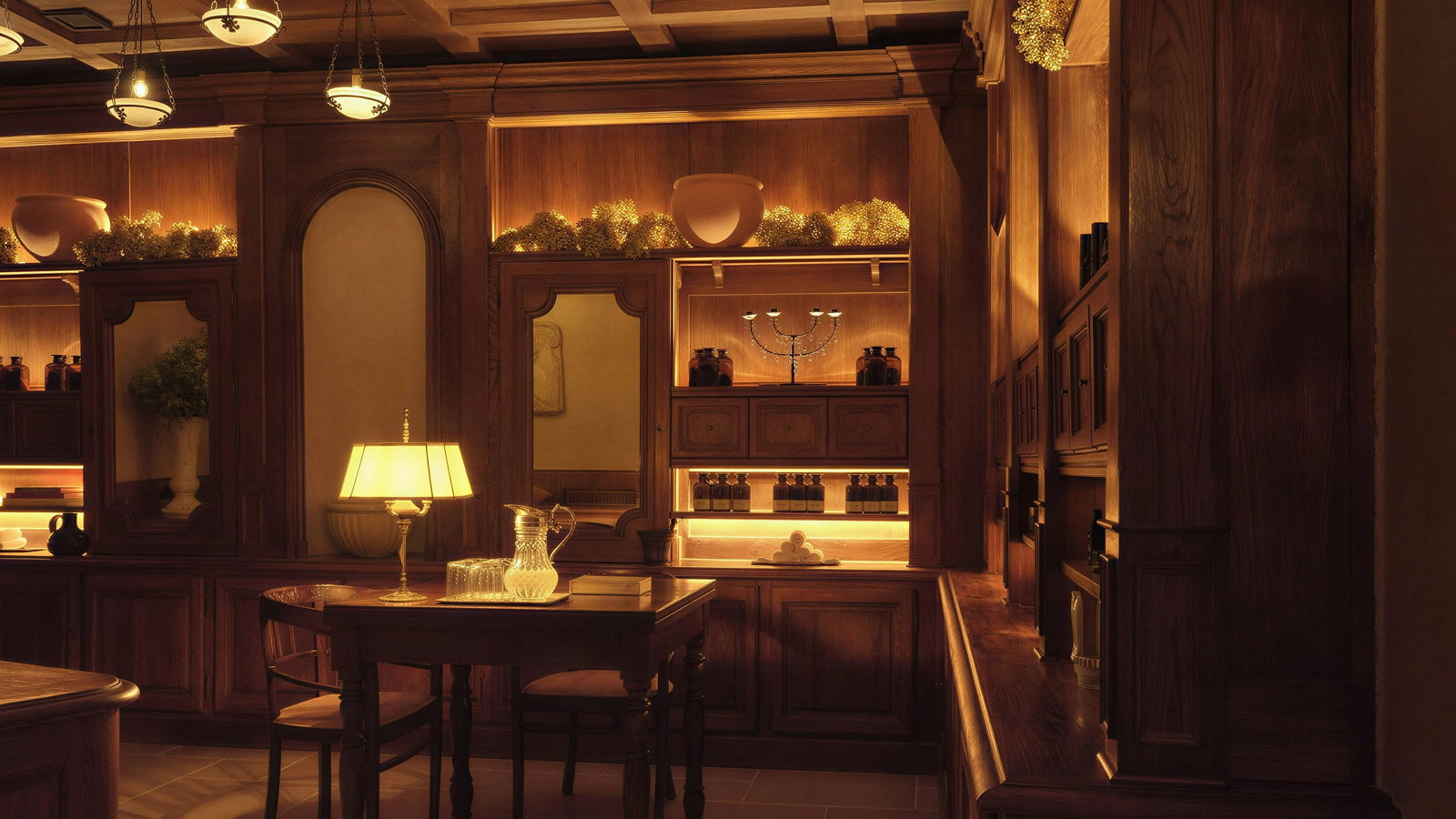 Reception desk at Hôtel du Couvent, set with lamp, glass pitcher, and books. Shelves hold decorative items. Cozy ambient lighting.