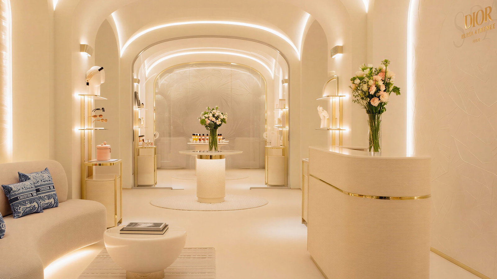 Elegant boutique Dior Spa Lobby interior at Hôtel Plaza Athénée with soft beige and gold tones. Flowers on central table. Dior sign on wall. Curved archways and plush seating.