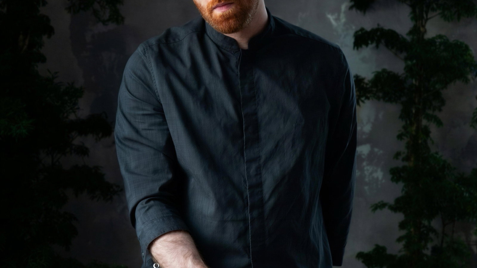 A person in a dark shirt holds a large ice shard over a glass. They appear focused, surrounded by greenery; gray background sets a calm mood.