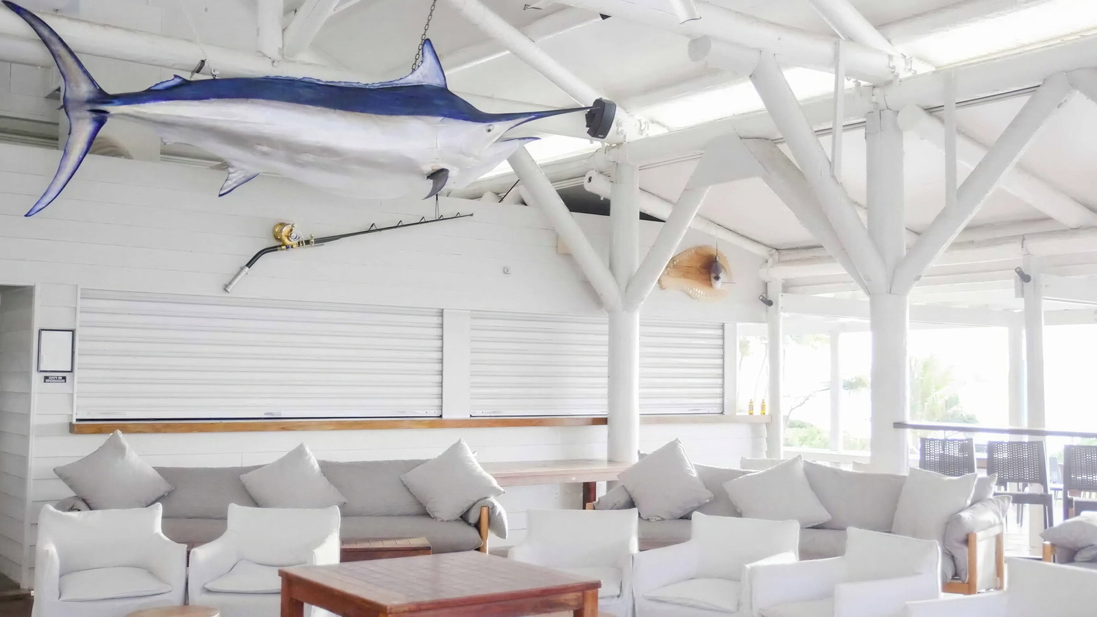 Marlin Bar interior at Lizard Island with white sofas, gray cushions, and a wooden table. A large fish model hangs from the ceiling. Bright, airy setting.