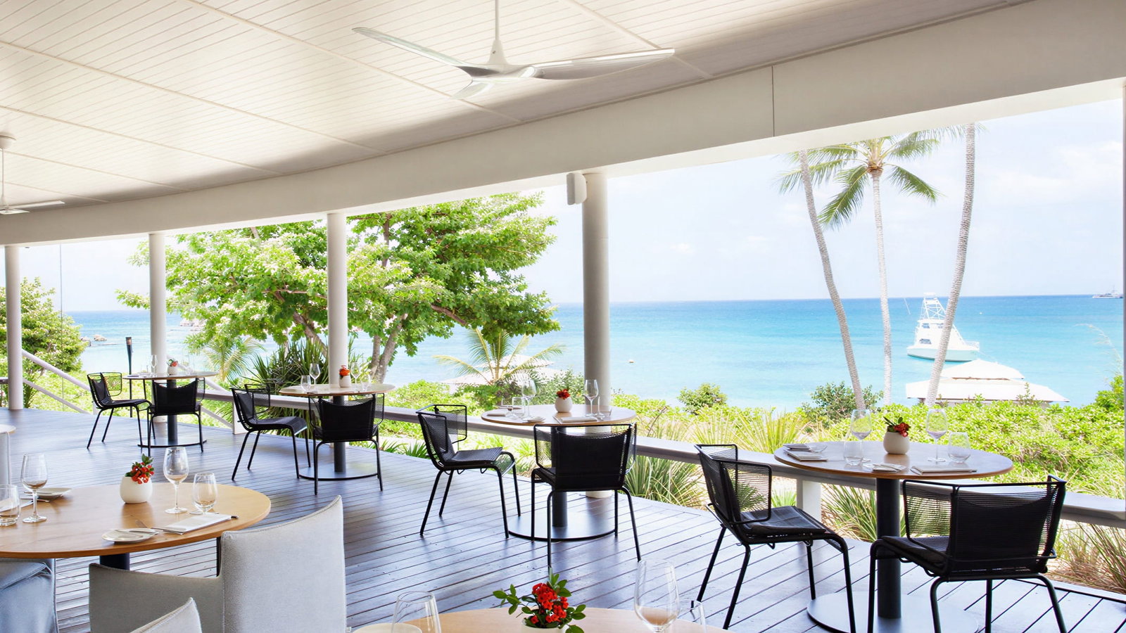 Salt Water Restaurant View at Lizard Island Resort with round tables and chairs, overlooking a bright blue ocean. Palm trees and greenery enhance the serene, tropical vibe.