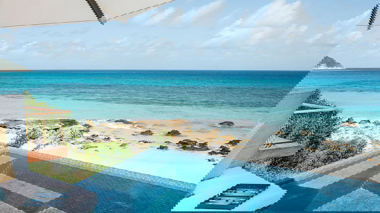 The House Lizard Island pool overlooking private beach with cushions under a large umbrella, under a blue sky