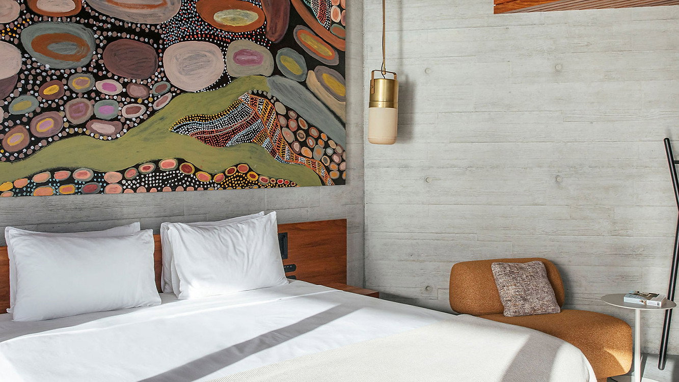 The House bedroom at Lizard Island with a large abstract painting above a bed. White linens, wooden accents, a cozy chair, and ladder decor add warmth.