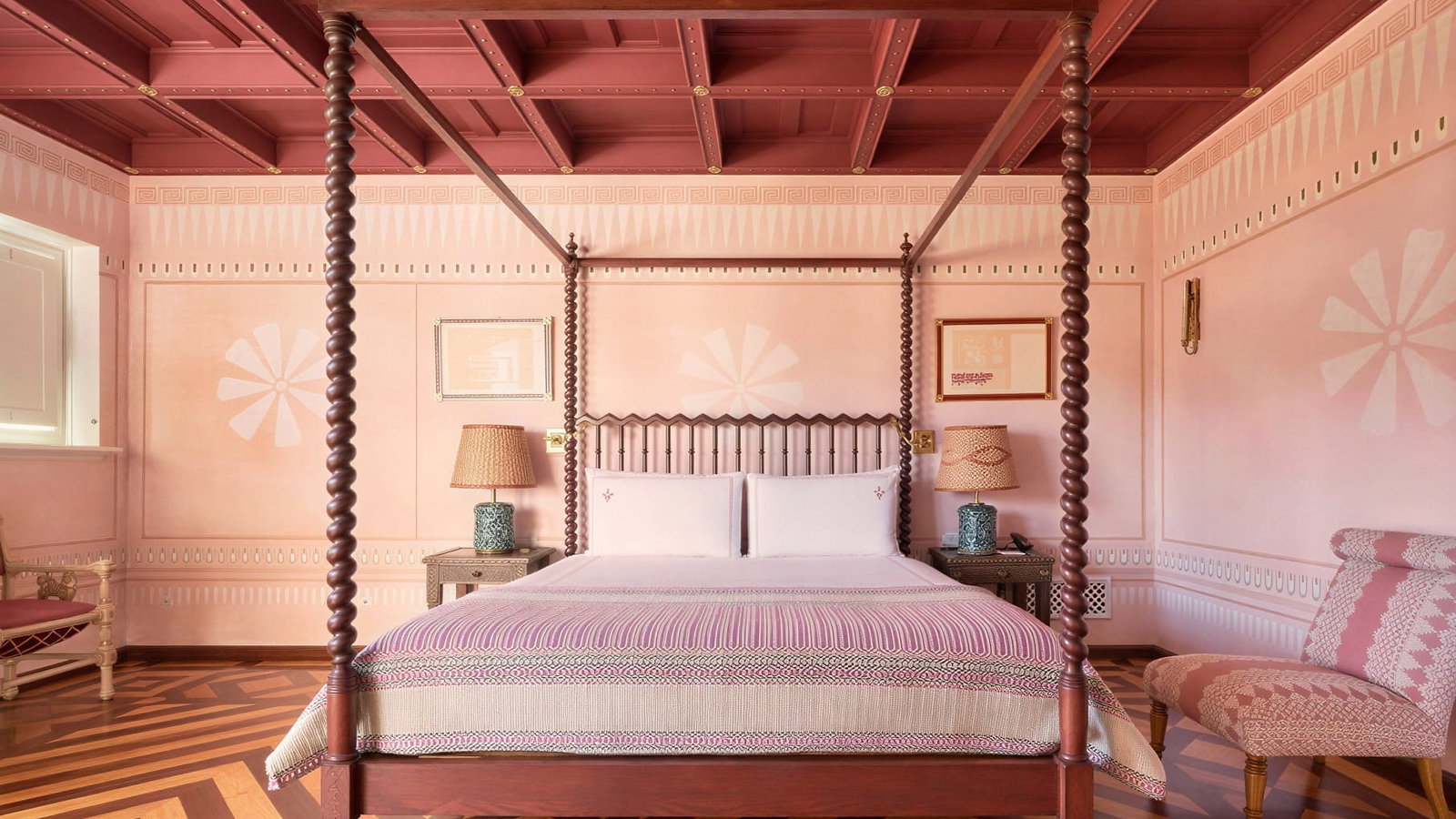 Matinha Suite ink-themed bedroom at Vermelho Melides with a four-poster bed, patterned throw, and geometric floor. Decorative chairs flank the bed, creating a cozy atmosphere.