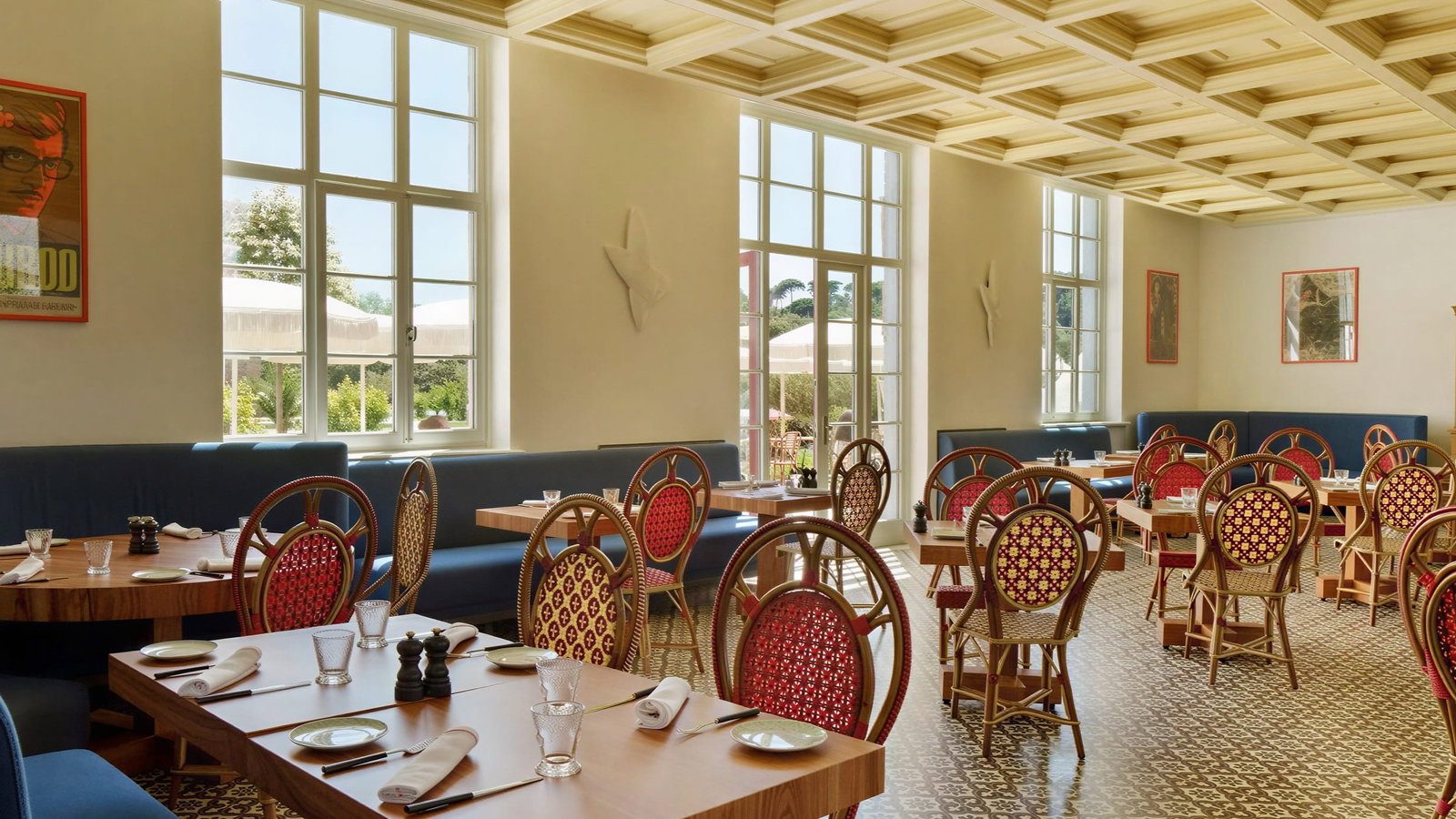 Restaurant Xtian dining room at Vermelho Melides with red-patterned chairs and wooden tables set for dining. Large windows and art on walls, creating a cozy atmosphere.