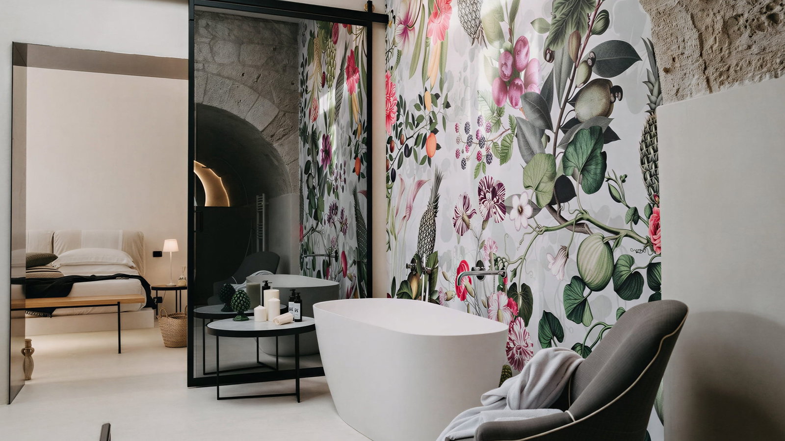 Deluxe Suite bathroom at Masseria Susafa with a floral mural, freestanding tub, chair, and candles. Neutral tones and natural light create a serene atmosphere.