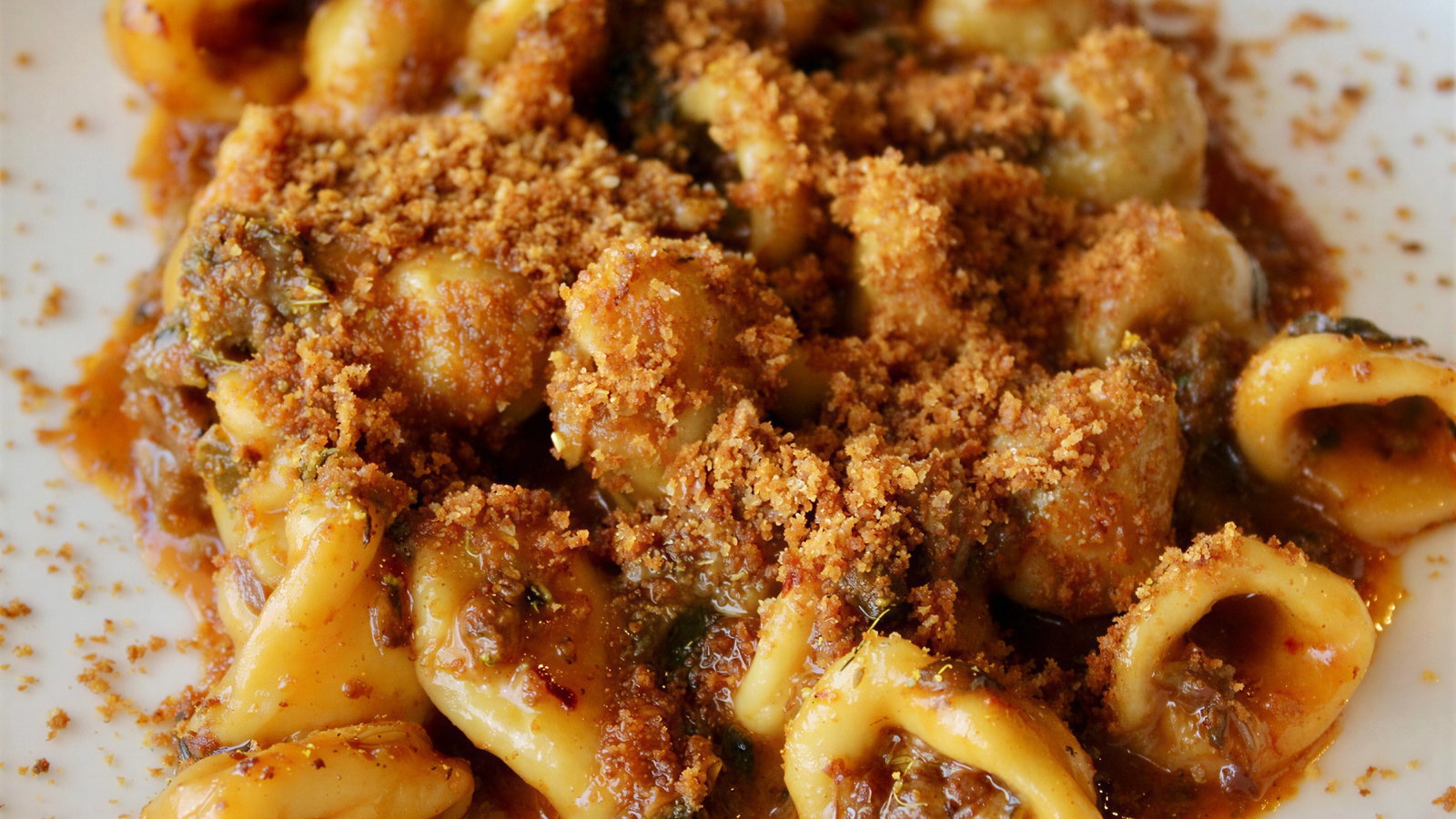 Close-up of tortellini in a rich, red sauce, topped with golden breadcrumbs on a white plate, creating a warm, appetizing appearance.
