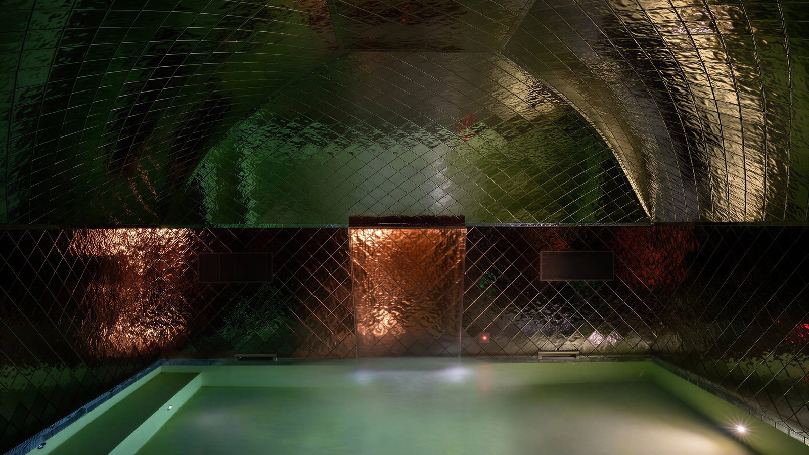 Dimly lit experiental swimming pool room at Palazzo Talìa with reflective green and copper tiles. A tranquil pool in the foreground creates a serene, mysterious atmosphere.