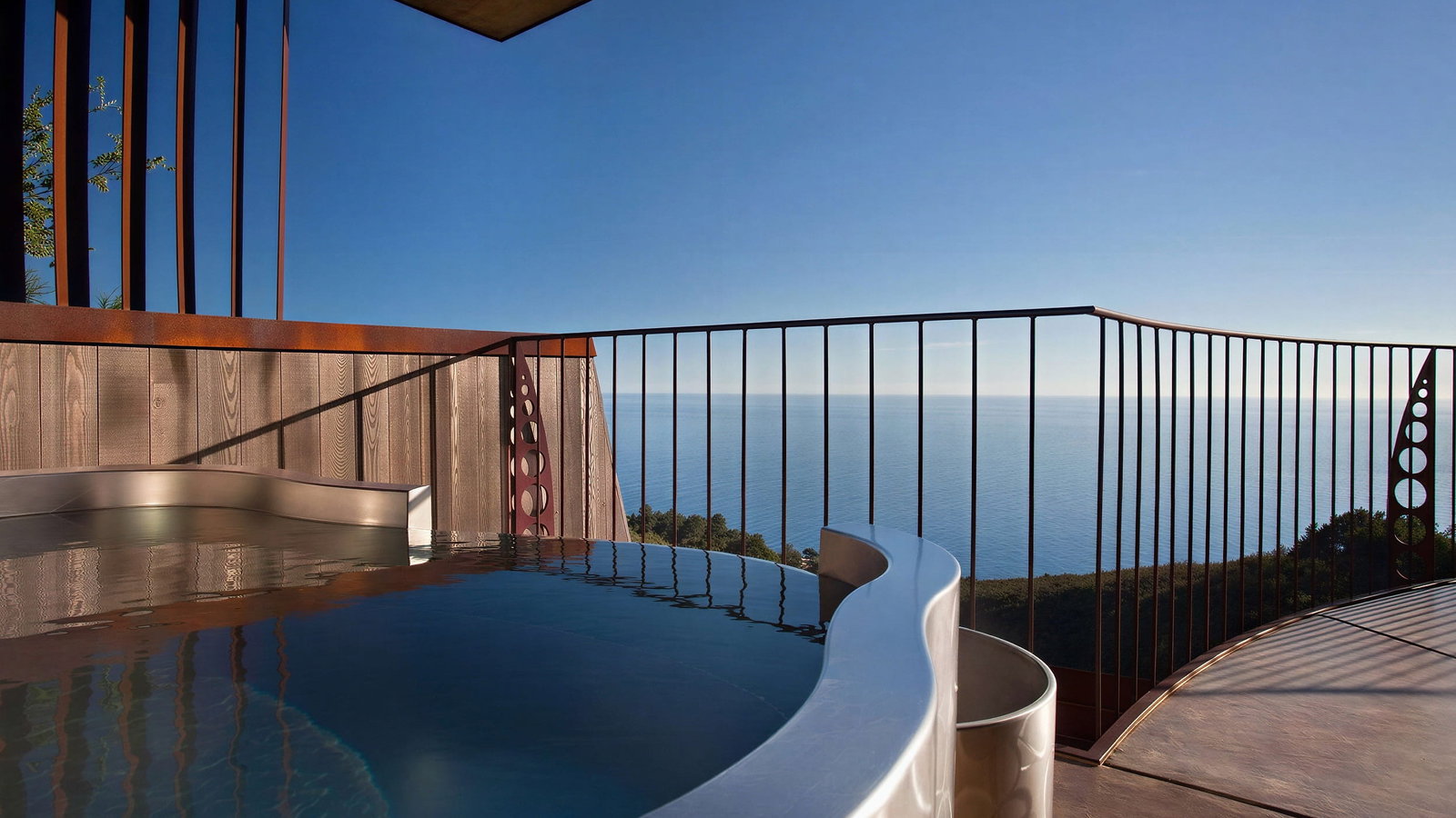 Pacific Suite outdoor hot tub at Post Ranch Inn with wood and metal railings overlooks a serene ocean view under a clear blue sky. Tranquil and luxurious setting.