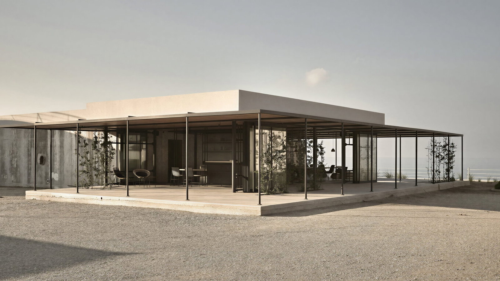 Reception at Dexamenes Seaside Hotel in a modern minimalist house with no walls, metallic frame, and open terrace. Sparse desert landscape and ocean visible in the background.