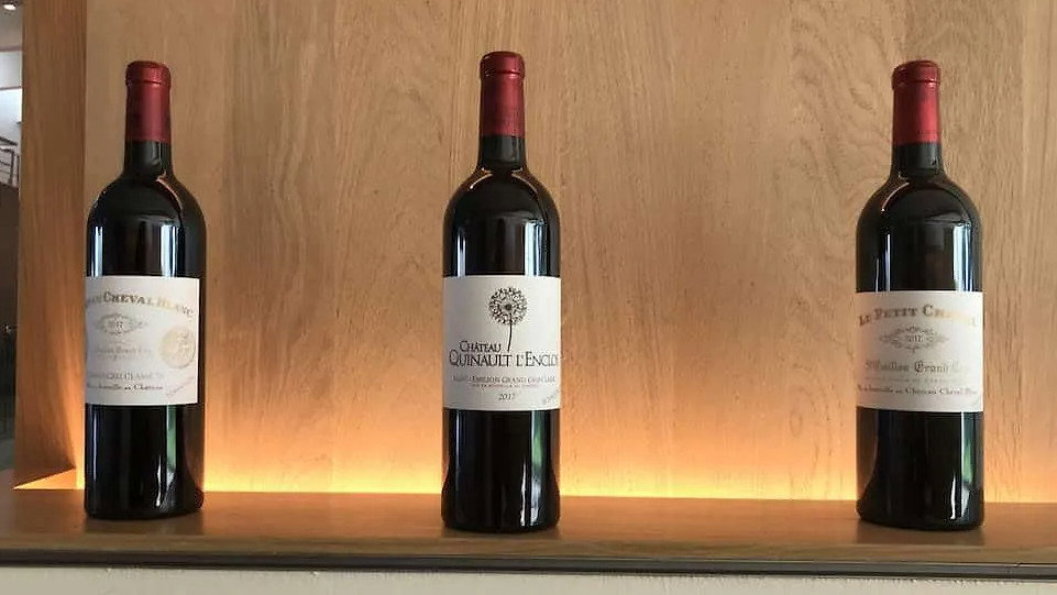 Three Château Cheval Blanc wine bottles with red caps are displayed on a backlit wooden shelf. Labels feature vineyards' names and vintage years, creating a refined ambiance.