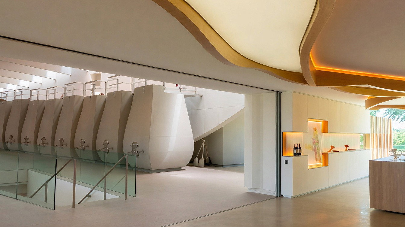 Modern winery vat room interior at Château Cheval Blanc with sleek metal fermentation tanks, curved ceiling, soft lighting, and a glass wall overlooking greenery.
