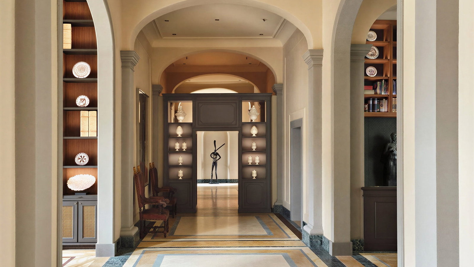Elegant Lobby hallway at Collegio alla Querce with arched ceilings, patterned marble floors, and displayed statues. Warm lighting creates a serene, sophisticated atmosphere.