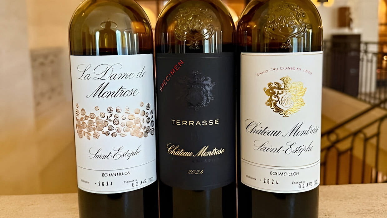 Three tasting wine bottles from Château Montrose with red caps on a stone surface inside an arched building. Labels read La Dame de Montrose, Terrasse, and Château Montrose.