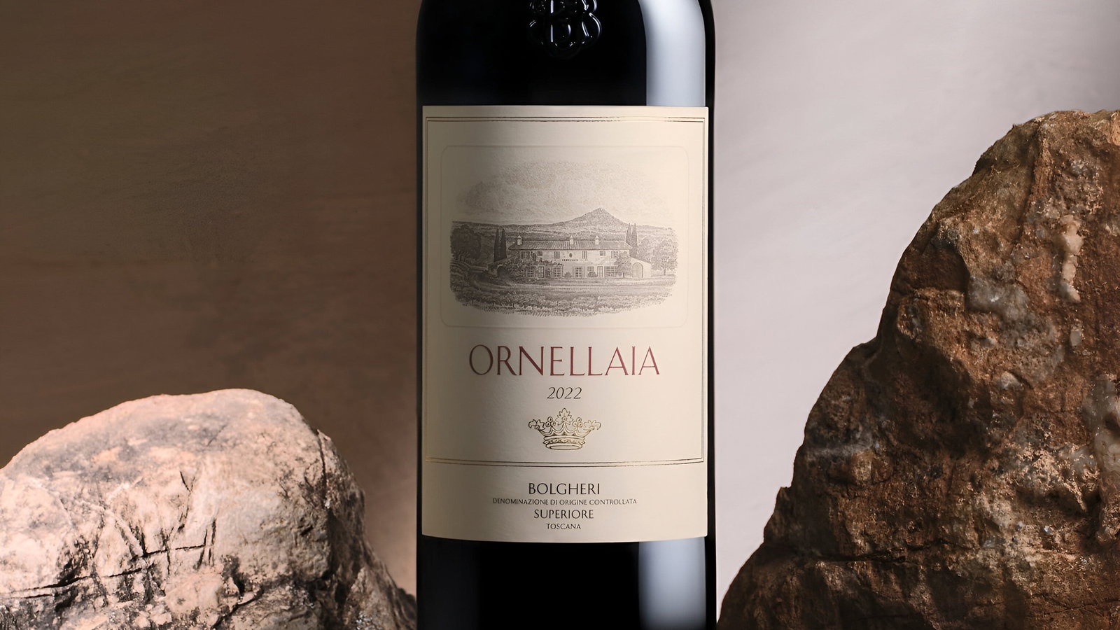 Wine bottle labeled "Ornellaia 2022" stands among rustic stones on a neutral background, conveying elegance and luxury.