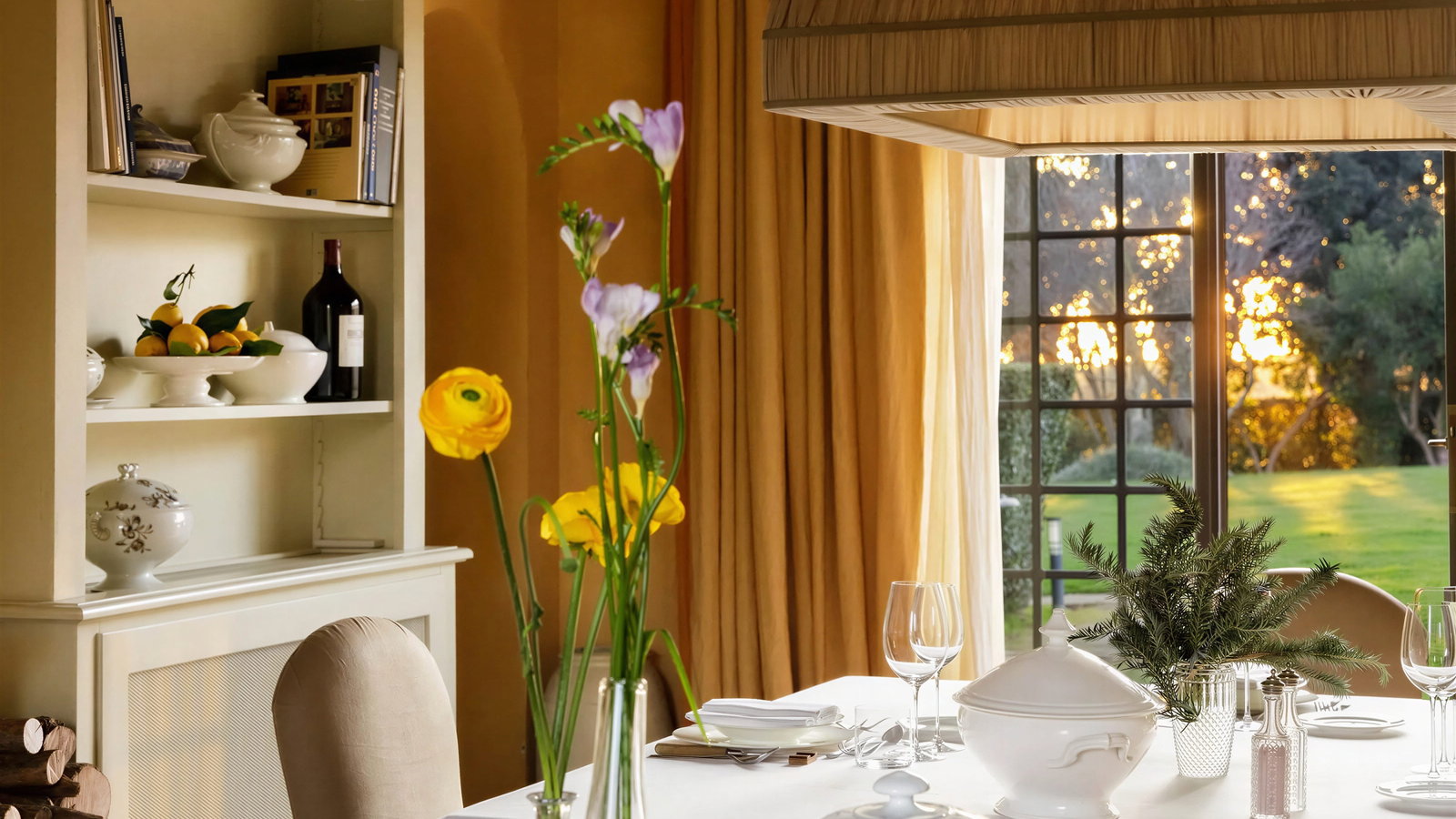 Elegant Ornellaia wine dinner tasting room with white tablecloth, plates, and glassware. Yellow flowers in vase, open window view of sunset over green lawn. Cozy ambiance.