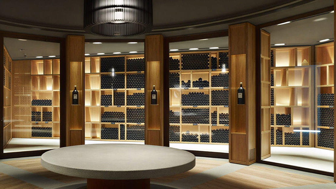 Luxurious Ornellaia Winery historical cellar with wooden shelves filled with bottles, ambient lighting, round table, and a large black-and-white wall art piece.