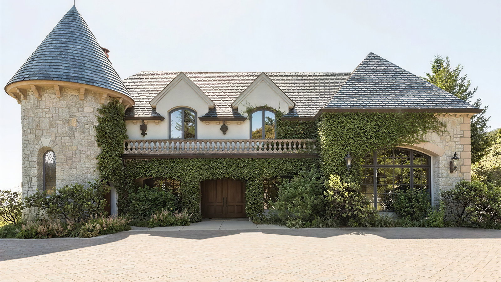 Stone house with ivy-covered walls, conical tower, arched windows, and a wooden door. Paved driveway and greenery in the foreground.