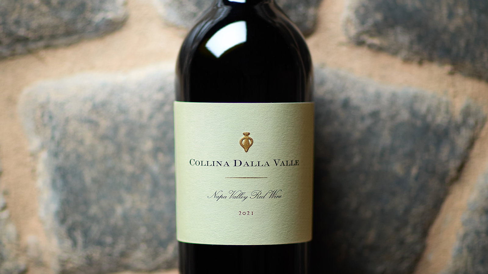 Bottle of red wine labeled "Collina Dalla Valle 2021" against a rustic stone background. The label is cream-colored with black text.