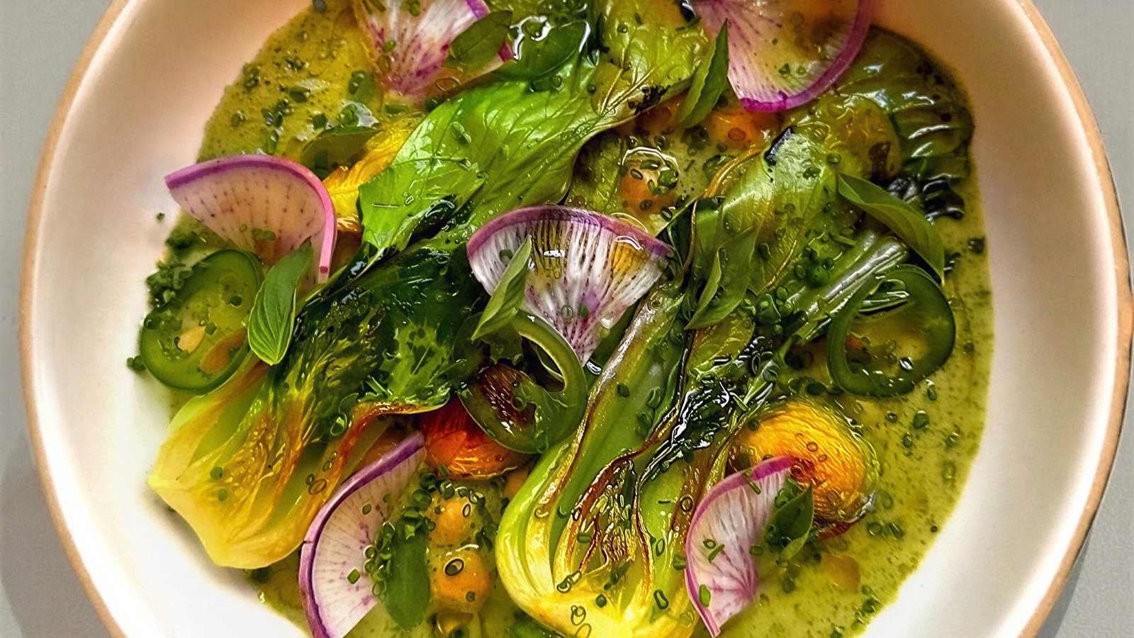 Salad featuring vibrant greens, radish slices, and jalapeños in a creamy sauce, served in a white bowl, creating a fresh, appetizing look.