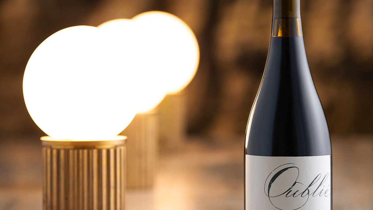 Wine bottle labeled "Oublie" on a marble surface, with warm glowing lights in the background creating an elegant, cozy atmosphere.