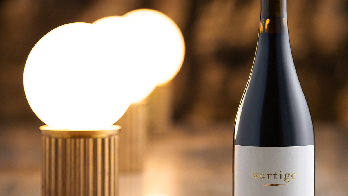 Wine bottle labeled "vertigo" on a reflective surface with glowing round lights in the background, creating a warm, elegant ambiance.
