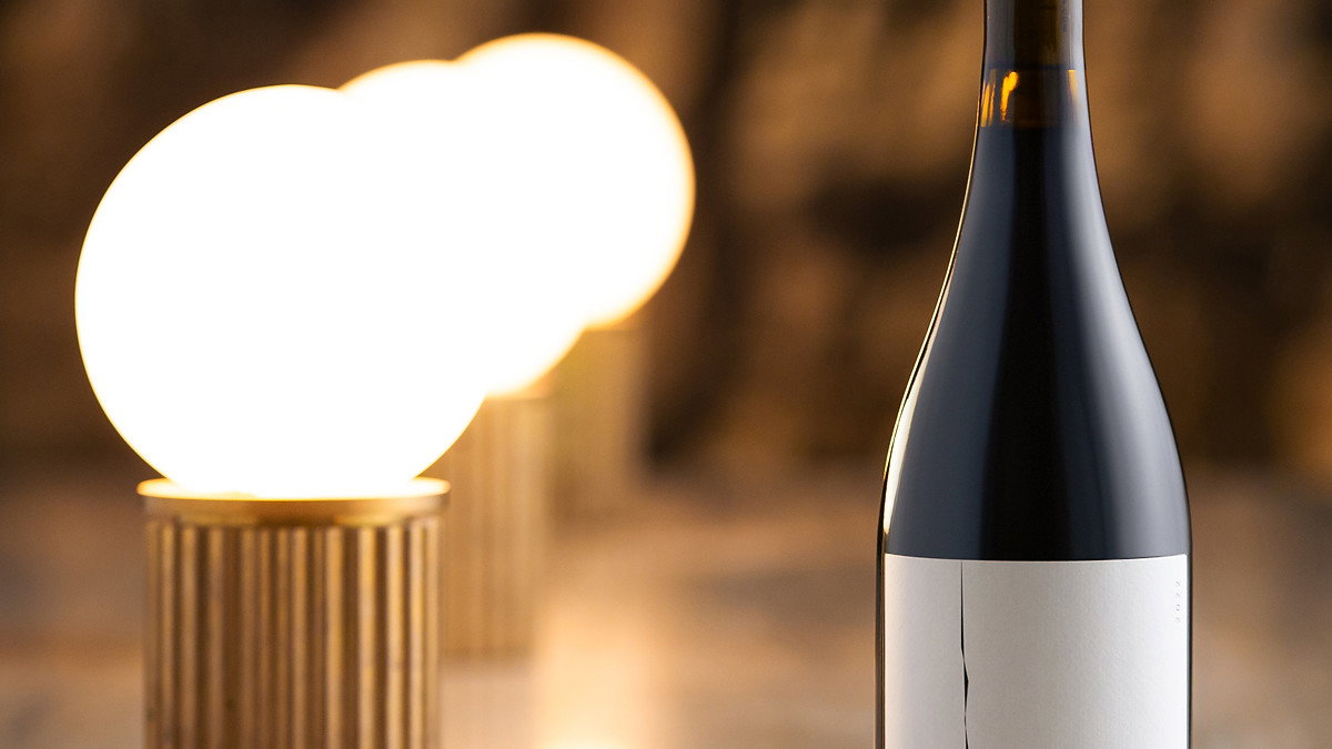 A wine bottle labeled "Fracture" sits on a reflective surface with glowing round lamps and a blurred warm-toned background.