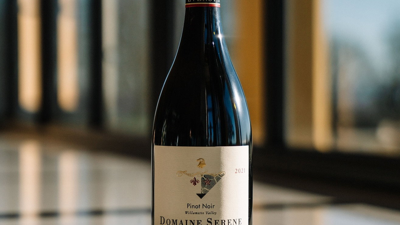 A bottle of Domaine Serene Pinot Noir on a marble table with a sunny, blurred window background. The label reads “Evenstad Reserve 2021.”