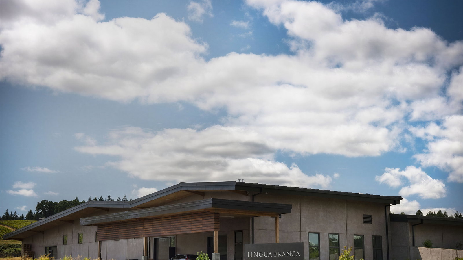 Modern building labeled Lingua Franca under a partly cloudy sky, surrounded by greenery. Calm and peaceful rural setting.