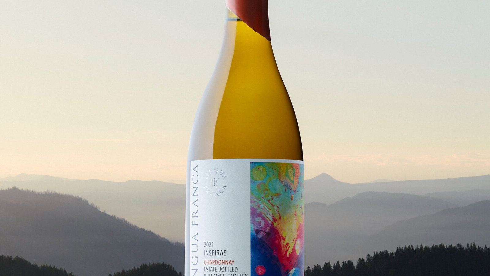 A wine bottle with a colorful label stands in front of a serene mountain landscape at dusk. Text reads: Lingua Franca, 2021 Chardonnay.