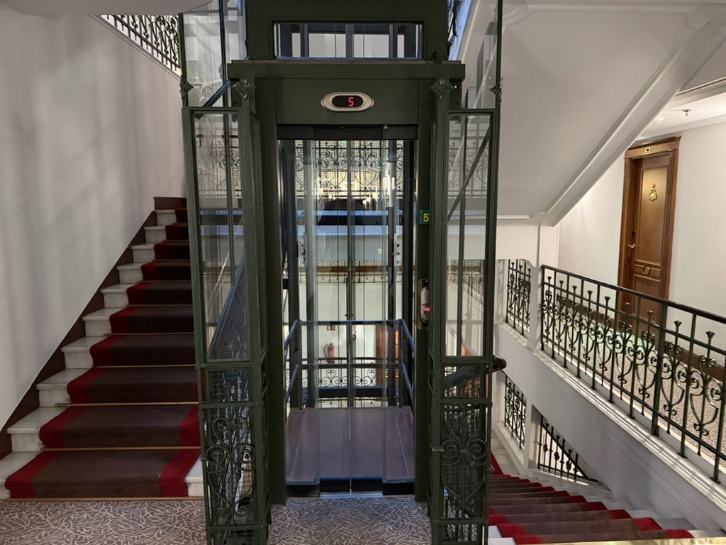 Classic green elevator and red-carpeted staircase at Hotel de Londres y de Inglaterra